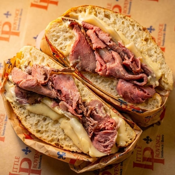 Two halves of a Little Provence roast beef and cheese sandwich on branded paper.